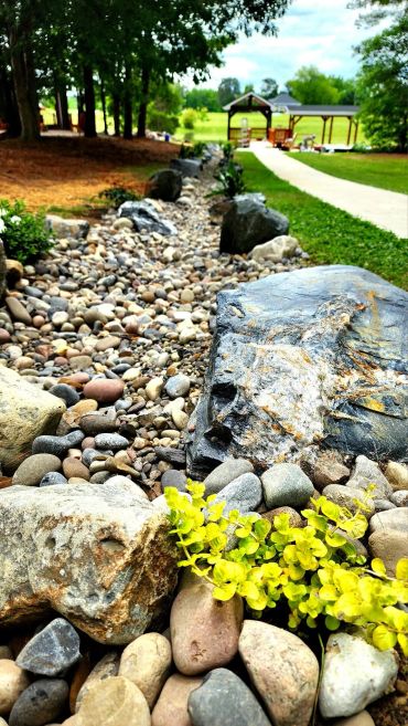 Rock-lined garden path with greenery and a pavilion in the background in Zebulon NC
