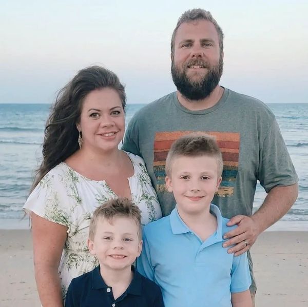 Family of four posing on the beach at sunset.