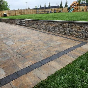 Backyard with paved patio and stone retaining wall.