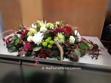 Whimsical funeral flowers in a casket spray created by a qualified florist
