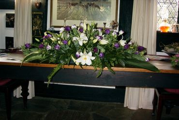 Purple and white flowers in a funeral casket spray created by a qualified florist