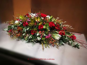 Red roses and native Australian flowers funeral casket spray flowers created by a qualified florist 