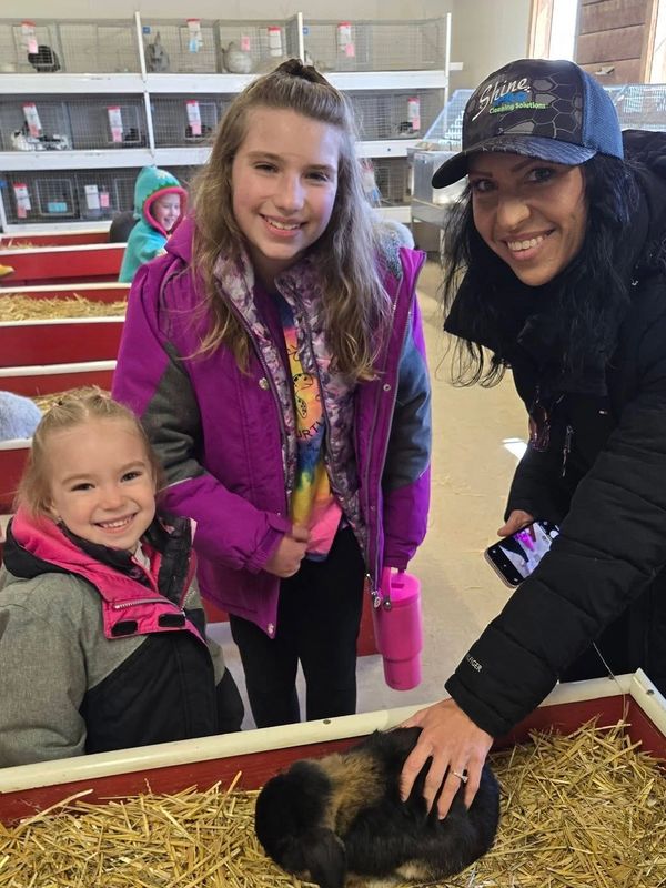 Three people smiling near a rabbit in an indoor petting area.
