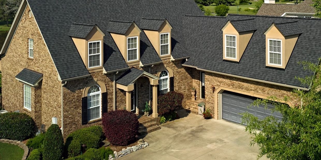 Elegant brick house with dark shingle roof and multiple dormer windows.