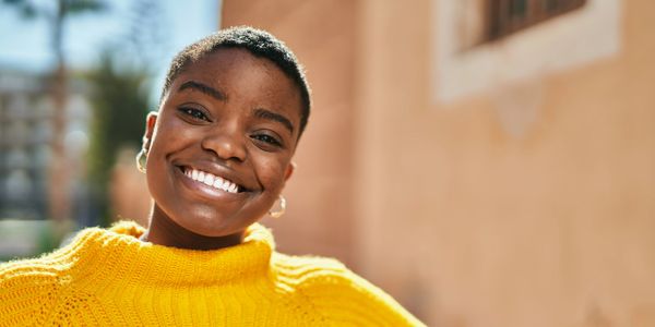 Young african-american female, smiling towards the camera while sitting outside in the sunshine.