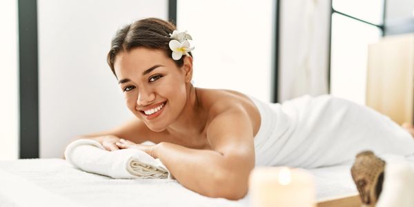 young woman laying on a massage table on her stomach, proped up and smiling at the camera.
