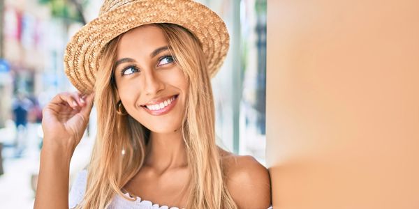 Young woman with a straw had and glowing skin enjoying the sunny day on a busy street market.