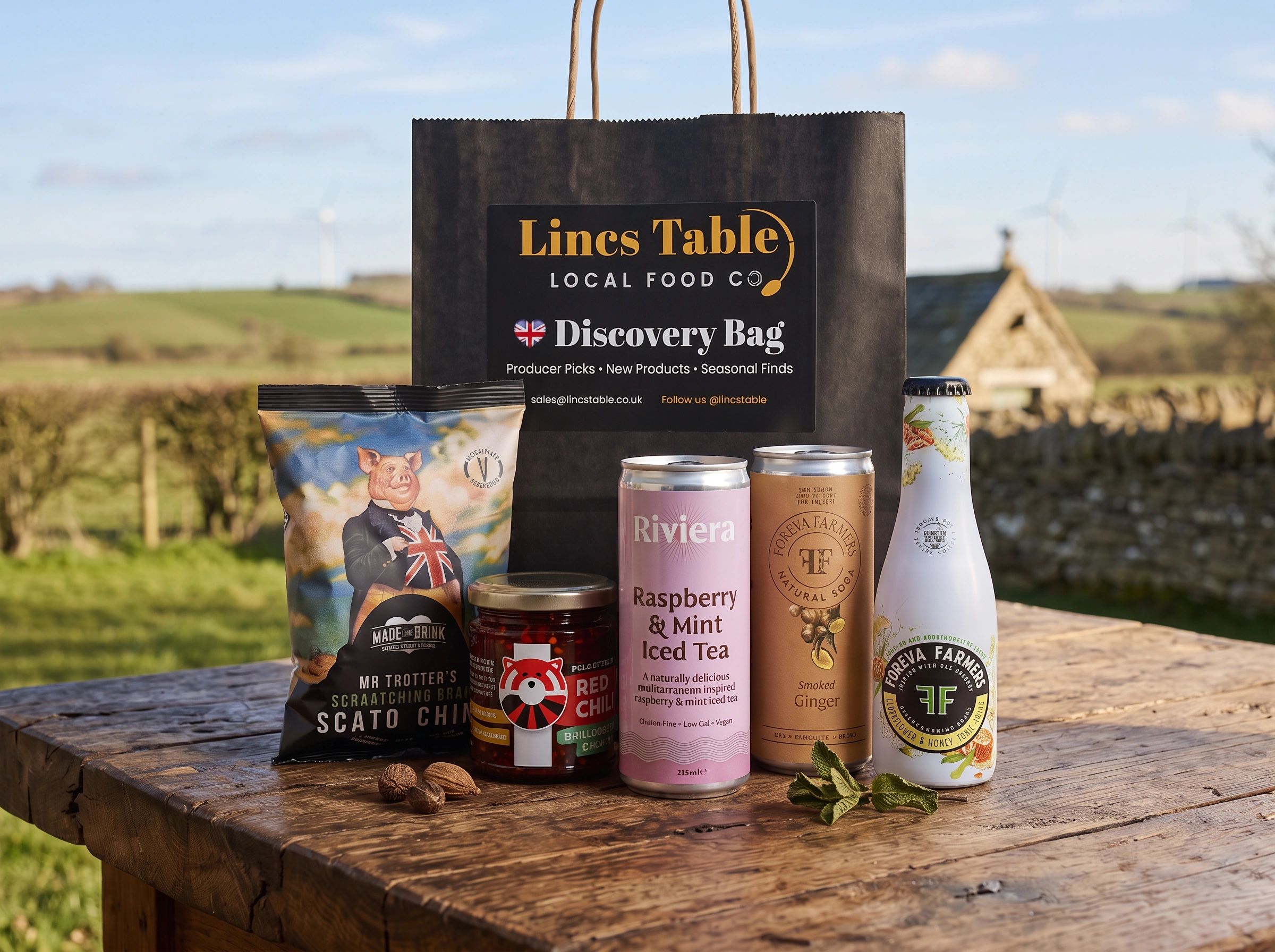 Local food and drink products displayed on a wooden table outdoors.