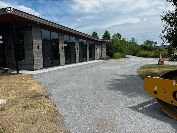Modern building with large glass windows beside a newly paved road and construction equipment.