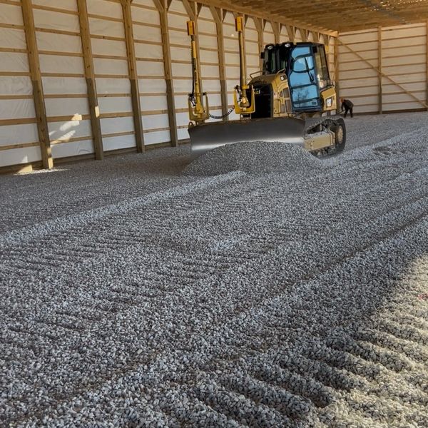 Bulldozer grading gravel inside a large wooden structure.