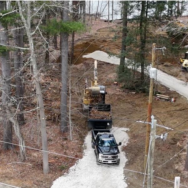 Construction vehicles working on a gravel path through a wooded area.