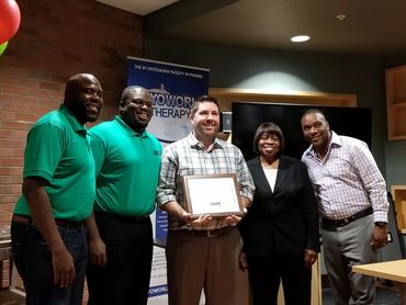 5 people standing together with one man in middle holding an award