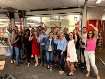 group of 17 people in a conference room standing up with arms in the air and smiling