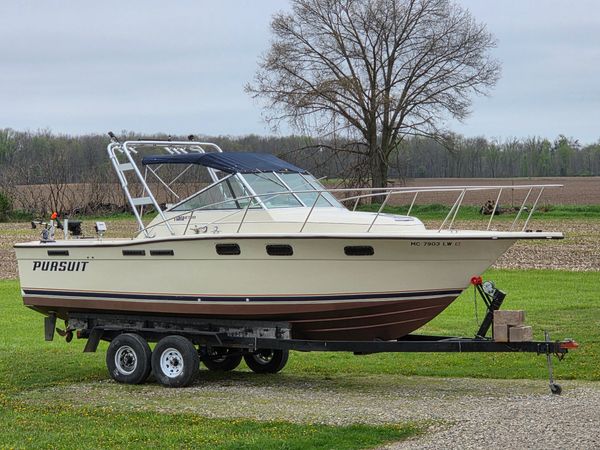 A beige Pursuit boat on a trailer parked on grass near a tree.