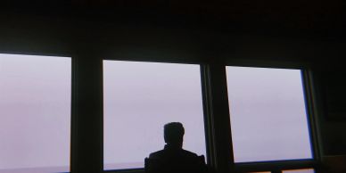 Silhouette of a person looking out of large windows at a foggy or cloudy sky.