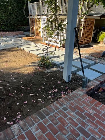 A garden with a cement walkway, a brick patio, and several trees.