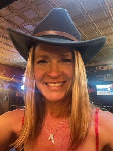 Smiling woman wearing a cowboy hat in a cozy, warmly lit bar.