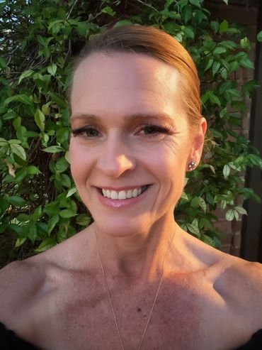 Smiling woman with earrings and necklace in natural light outdoors.