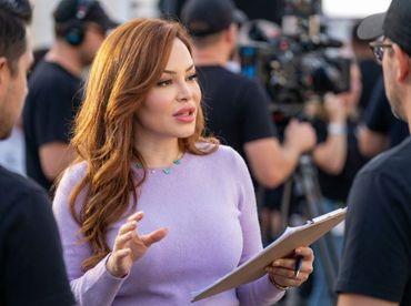 Woman in purple sweater discusses notes on set with crew during filming.