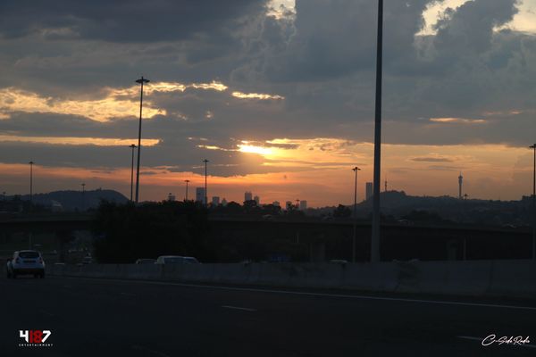 Sunset over a city skyline with a busy highway in the foreground.