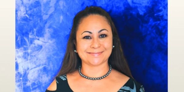 Smiling woman in patterned dress with blue background.