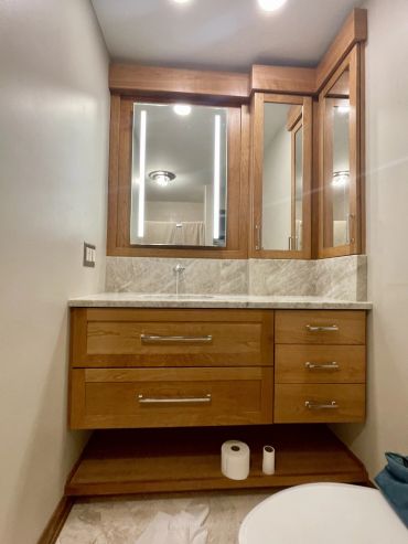 Modern bathroom vanity with wooden cabinets and illuminated mirror.