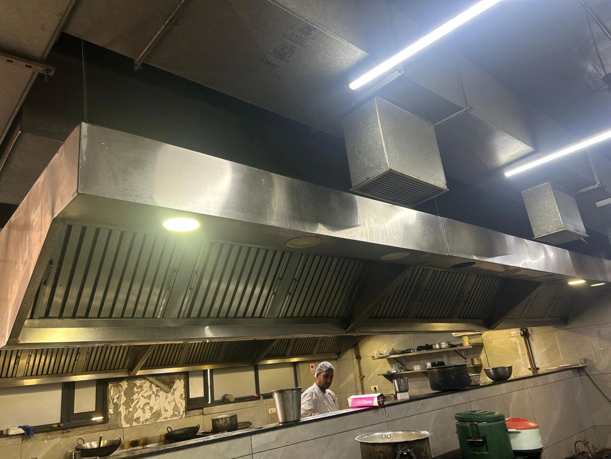 Chef working in a commercial kitchen with stainless steel ventilation.