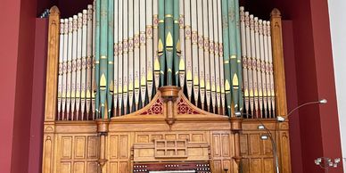Large pipe organ with wooden casing and polished floor in a red-walled room.