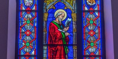 Stained glass window depicting a saint in red robes reading a book.