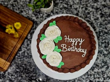 Chocolate birthday cake decorated with white flowers.