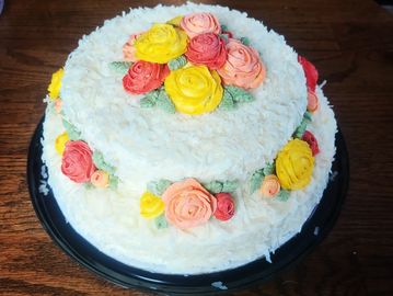 Two-tier white cake decorated with colorful buttercream roses.