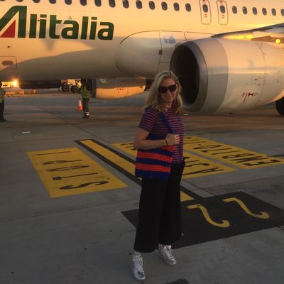 Woman posing near Alitalia airplane on runway at sunset.