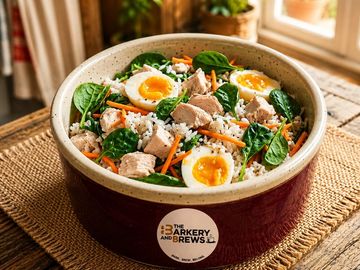 A bowl of rice with spinach, boiled eggs, carrots, and chunks of meat.