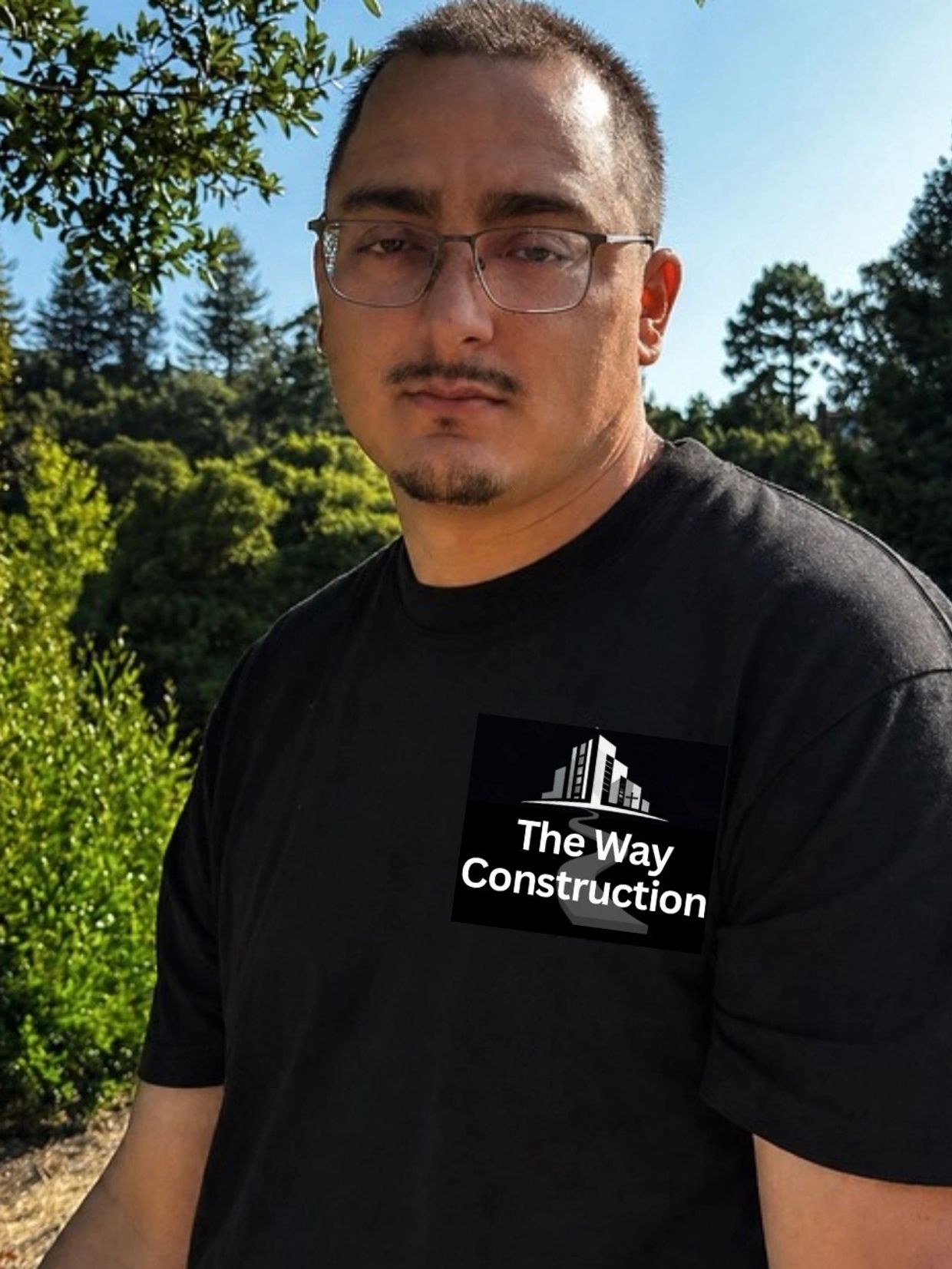 Man wearing a black t-shirt with 'The Way Construction' logo outdoors.