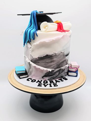 Graduation cake with a graduation cap and scroll on top, and books either side.