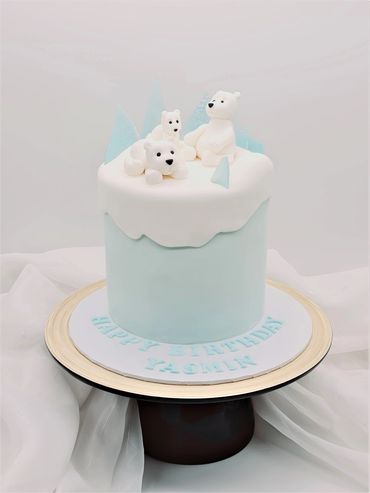 Light blue cake with white sugarpaste drapped over the top. Three polar bears sat on top of cake.