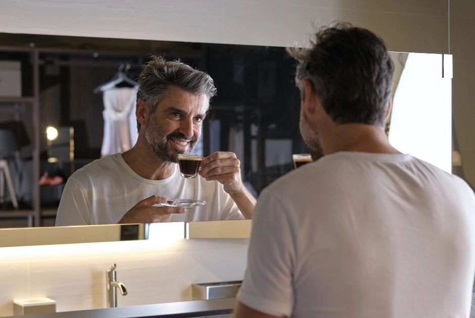 a man drinking coffee in his remodeled bathroom, looking in the mirror laughing & enjoying him self