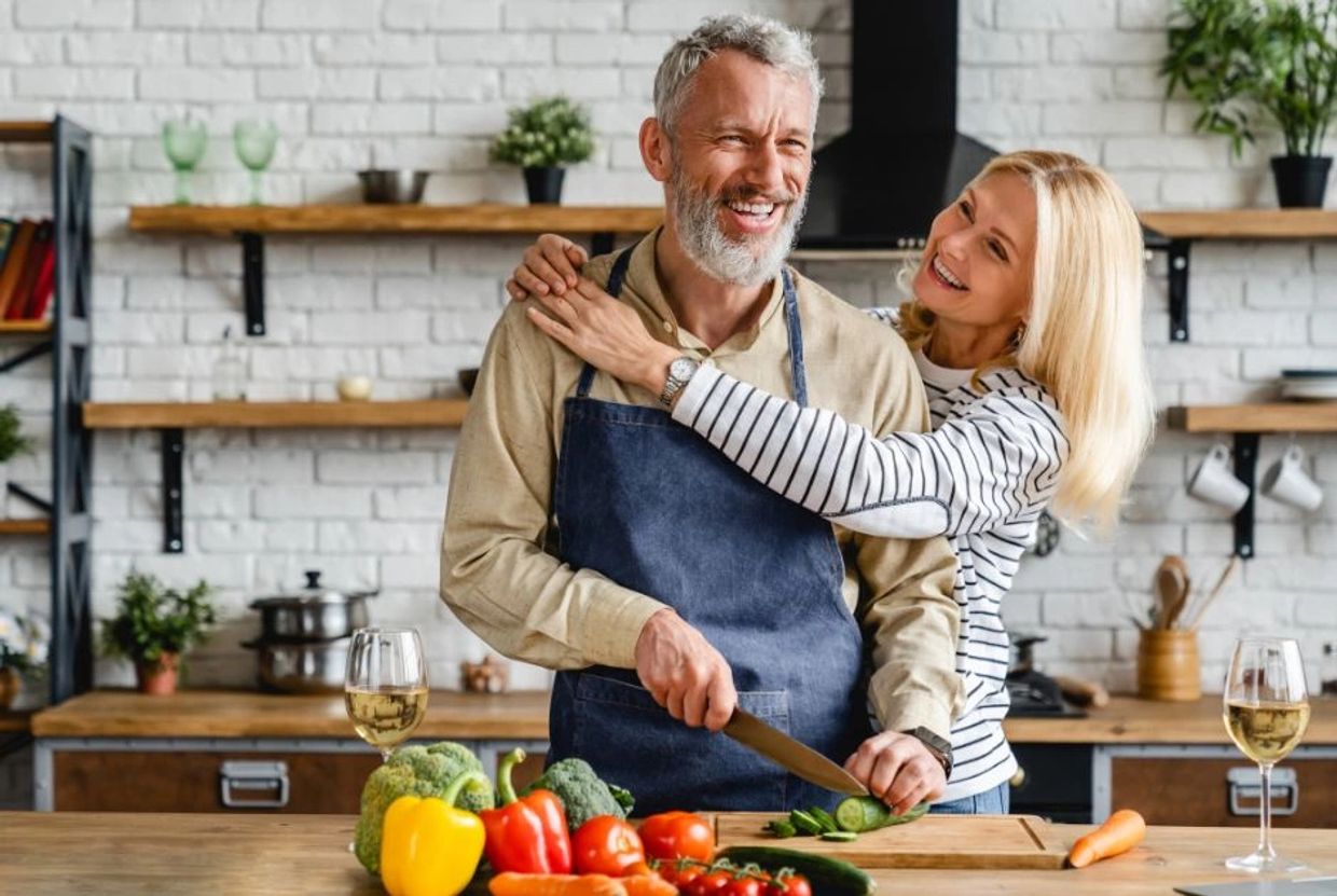 a mid aged man & woman cooking in their remodeled kitchen and laughing and enjoying