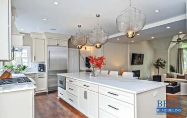 a remodeled kitchen with white cabinets & white quartz countertop, 3 pendant lights , wooden floor