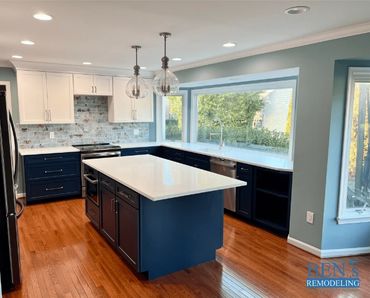 a remodeled kitchen with white & dark blue cabinets, white quartz countertop , wooden floor,