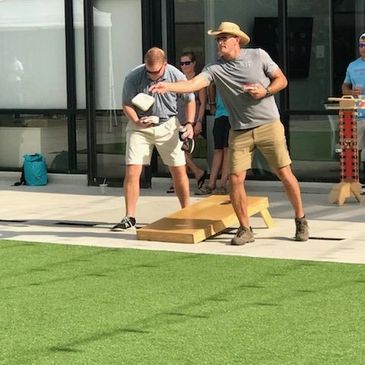 Two men playing cornhole outdoors on a sunny day.