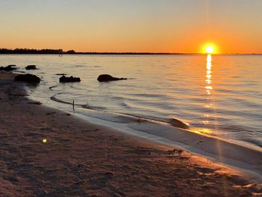 Sunset over a calm beach with gentle waves and rocks.