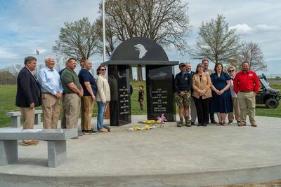 Group of people standing around a memorial monument with names inscribed.