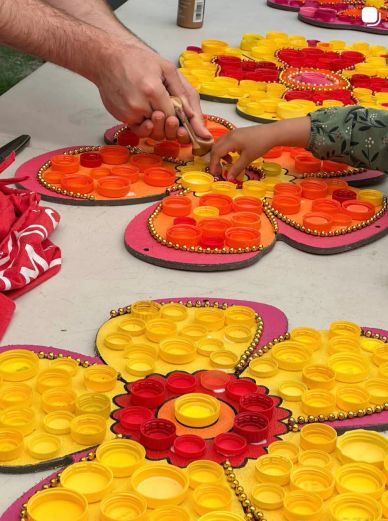 Hands arranging colorful bottle caps on flower-shaped boards.