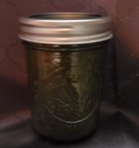 A glass jar filled with a dark green substance, sealed with a metal lid.