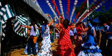 People dancing in colorful flamenco dresses at a vibrant outdoor festival.