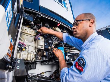 Technician repairing a truck engine, wearing safety glasses and a certified master patch.