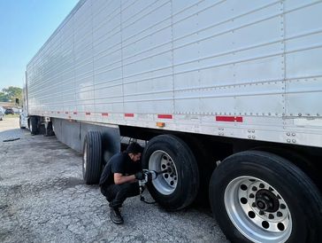 A man changes a tire on a large truck trailer outdoors.