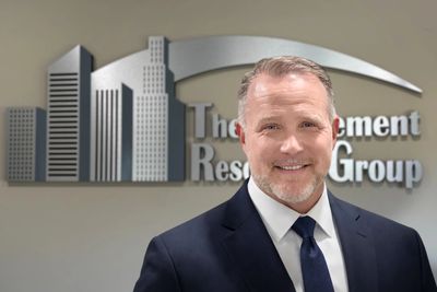 Professional man in suit smiling in front of a business logo.