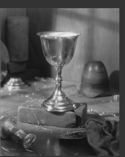 Pewter chalice brightly illuminated on a workshop bench.